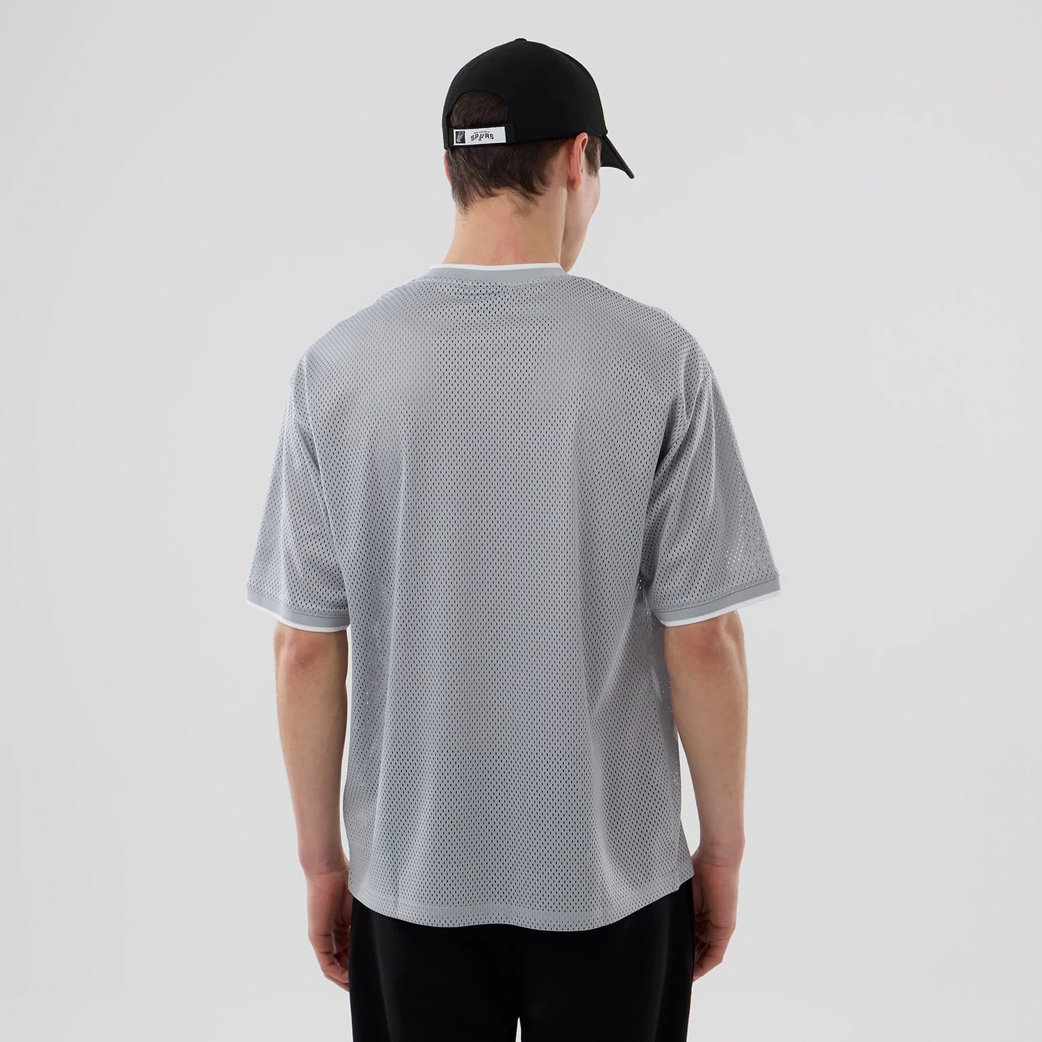New Era San Antonio Spurs NBA Mesh Grey Oversized T-Shirt, back view on-model showing the textured grey mesh fabric throughout, short sleeves with white trim, and a relaxed fit that complements the black cap worn by the model.
