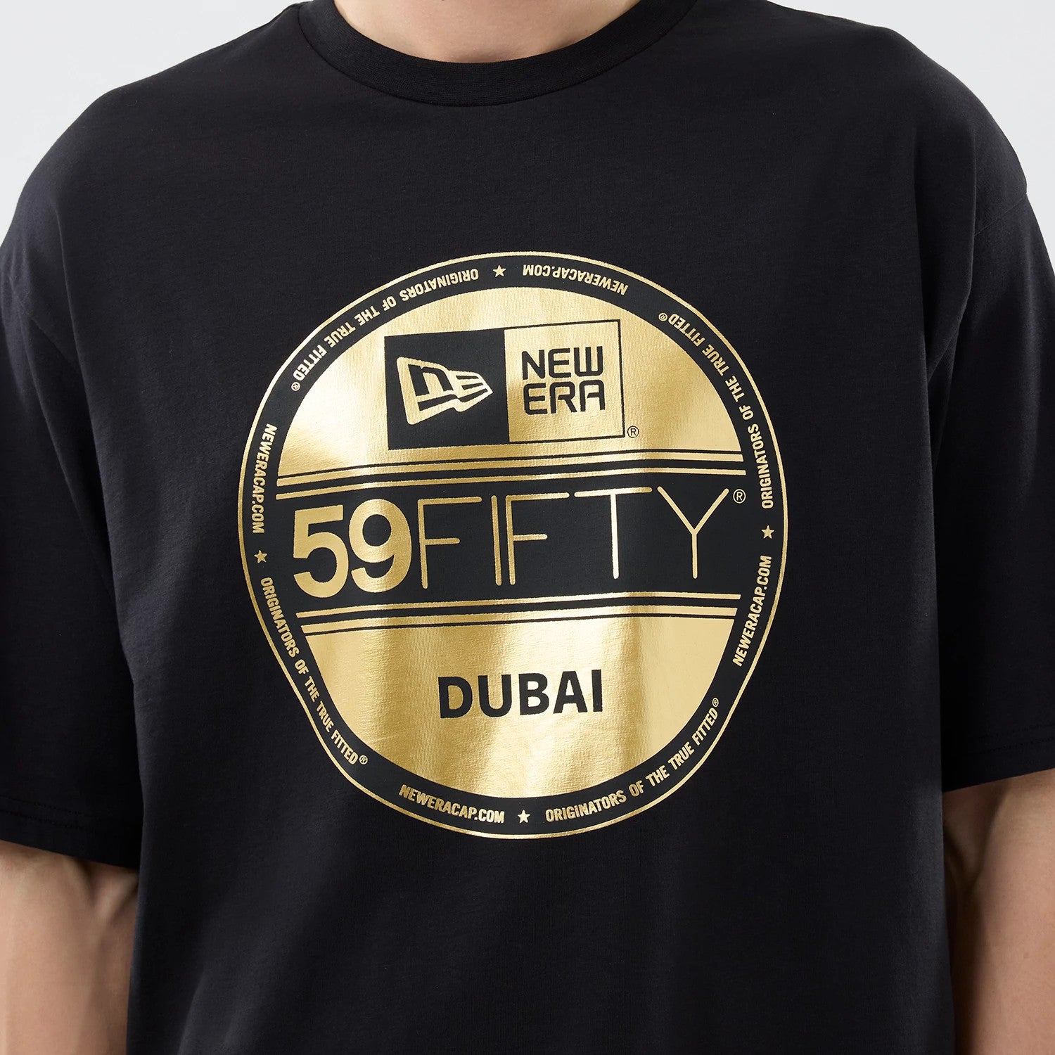 New Era Sticker Dubai Black Oversized T-Shirt, front view showcasing a large gold printed circular emblem on the chest with the 59FIFTY logo, New Era branding, and Dubai text, styled casually on a model.