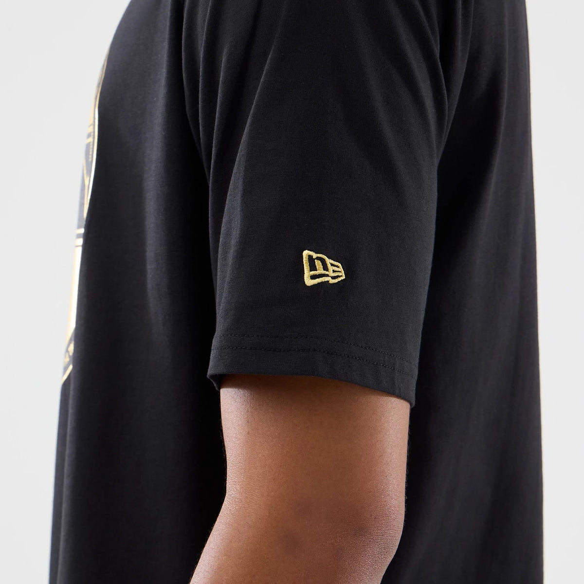 New Era Sticker Madrid Black Oversized T-Shirt, side view on-model featuring a short sleeve with an embroidered gold New Era logo near the hem, part of a larger graphic along the side of the garment.
