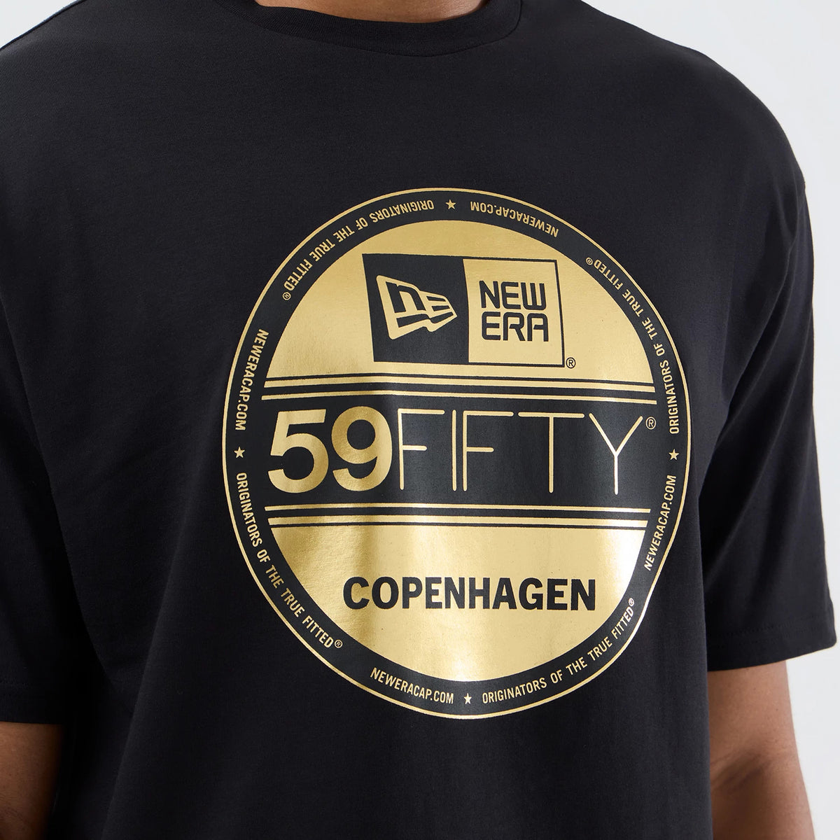 New Era Sticker Copenhagen Black Oversized T-Shirt, front view displaying a large gold printed 59FIFTY sticker graphic centred on the chest with the New Era logo on the left, against a plain black background in a relaxed fit.