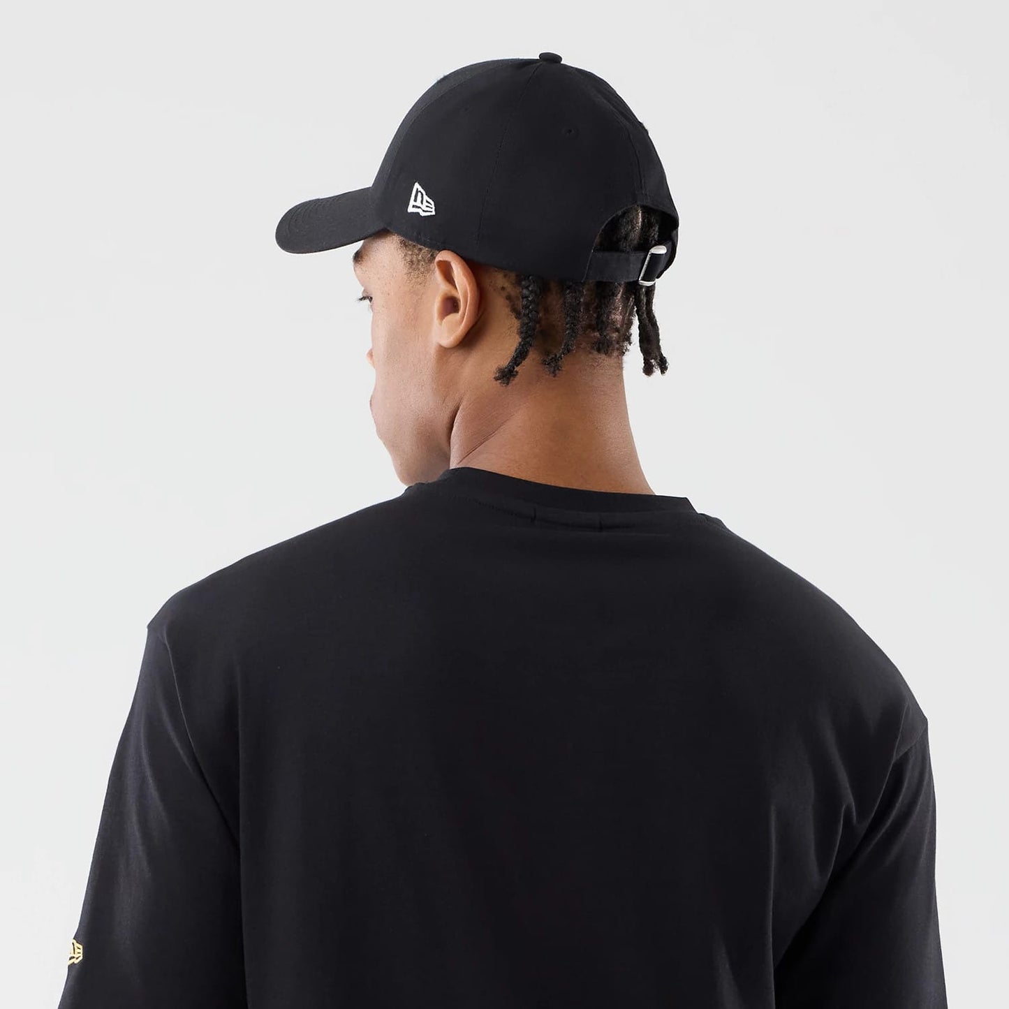 New Era Sticker Copenhagen Black Oversized T-Shirt, rear view on a model wearing a black cap, showing the plain back of the T-shirt, a small yellow embroidered New Era logo on the left sleeve and a low-profile fit.