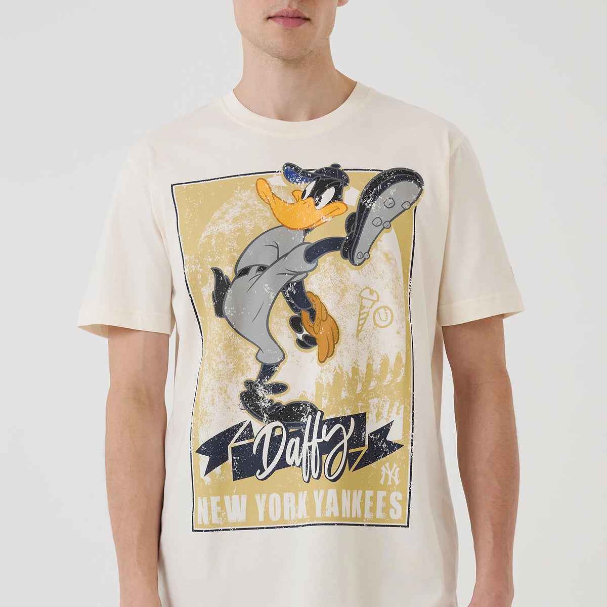 New Era New York Yankees MLB X Looney Tunes Cream T-Shirt, front view on-model featuring a large printed graphic of Daffy Duck in a baseball uniform, positioned centrally with Daffy and New York Yankees text below, and a New Era logo.