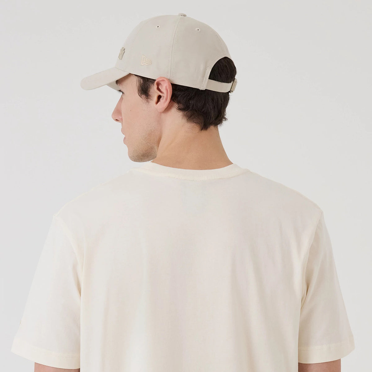 New Era New York Yankees MLB X Looney Tunes Cream T-Shirt, back view on-model featuring plain cream fabric with short sleeves, paired with a cream cap that has an embroidered New Era logo on the side and an adjustable strap at the back.