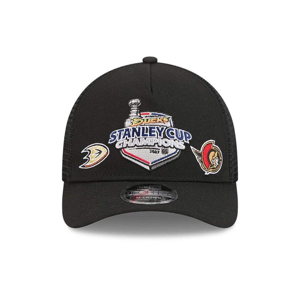 Ducks NHL Stanley Cup Black New Era 9FORTY M-Crown A-Frame Trucker Adjustable Cap, front view showing the embroidered Stanley Cup Champions logo centred on the black crown, with team logos on each side and a 9FORTY size sticker on the curved visor.