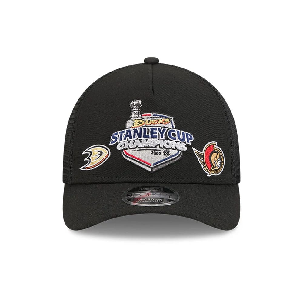 Ducks NHL Stanley Cup Black New Era 9FORTY M-Crown A-Frame Trucker Adjustable Cap, front view showing the embroidered Stanley Cup Champions logo centred on the black crown, with team logos on each side and a 9FORTY size sticker on the curved visor.