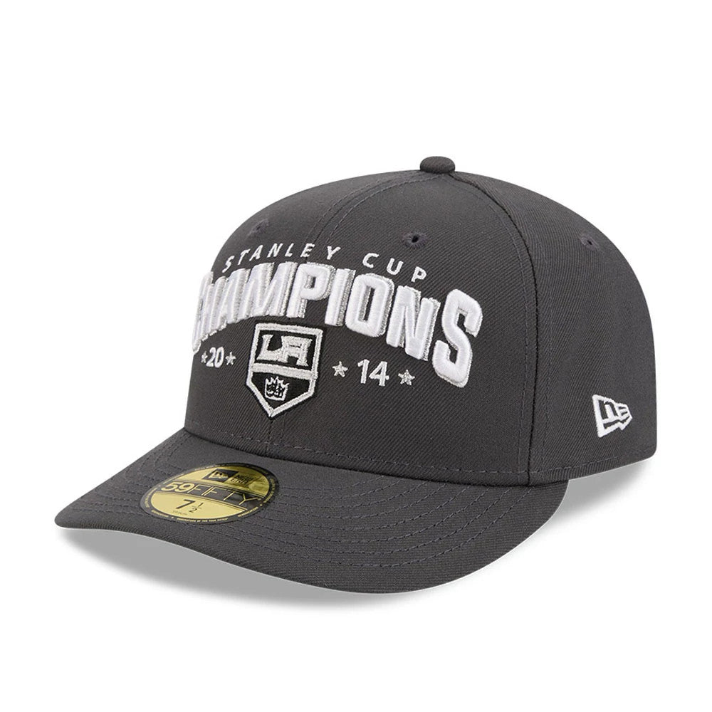 LA Kings NHL Stanley Cup Champions Dark Grey New Era 59FIFTY Fitted Cap, three-quarter view showing white embroidered 'Stanley Cup Champions' text across the front panel above the LA Kings emblem, with a flat visor and gold 59FIFTY size sticker.