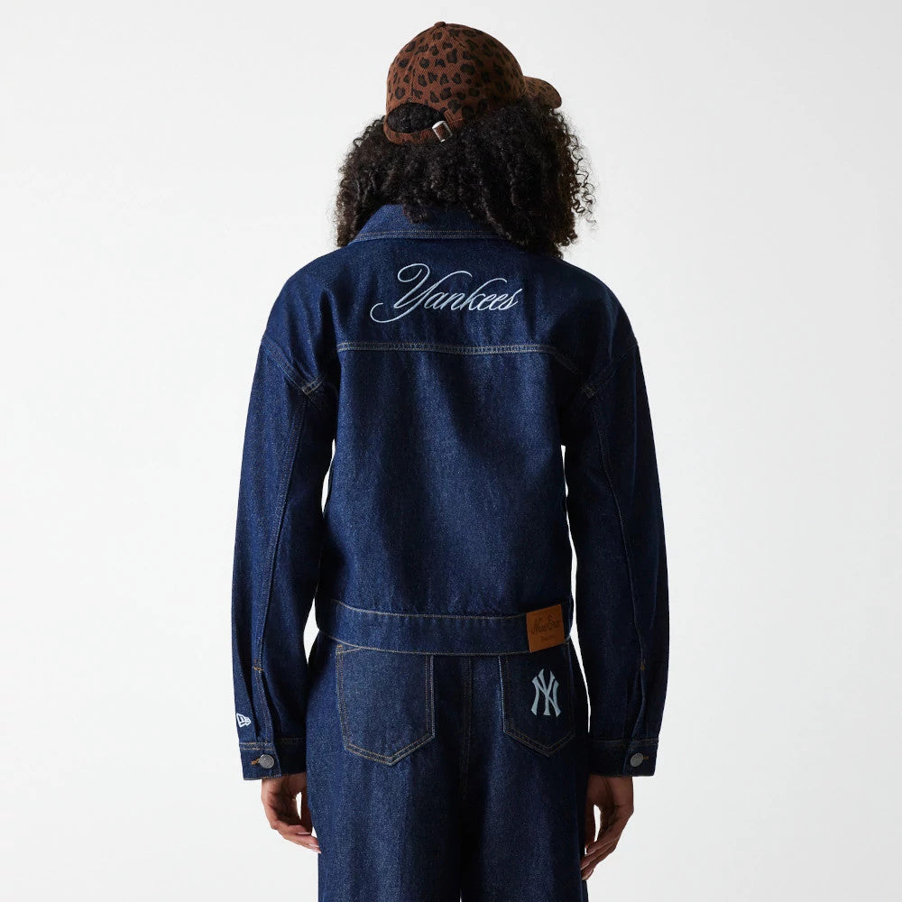 New Era New York Yankees Womens MLB Denim Dark Blue Jacket, back view on a model styled with jeans and a cap, featuring embroidered Yankees lettering across the upper back, an embroidered New York Yankees logo on the lower right.