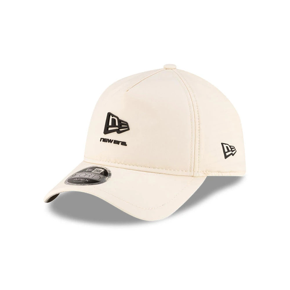 New Era Light Beige 9FORTY Apex Cap, three-quarter view showing the raised black New Era logo prominently embroidered on the front panel, black New Era flag logo on the left side, and a 9FORTY size sticker on the light beige curved visor.