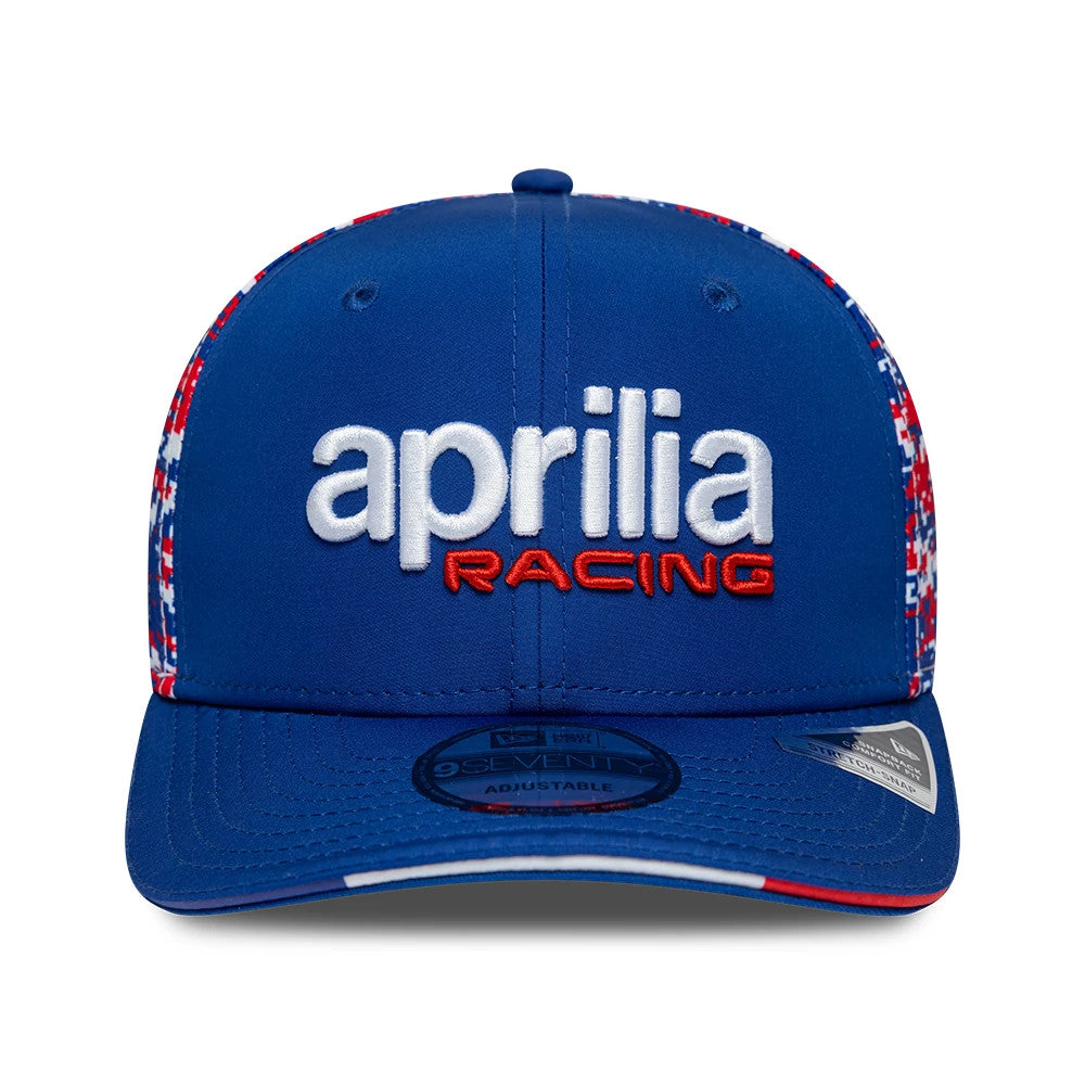 Aprilia Replica Le Mans Race Special Blue New Era 9SEVENTY Stretch Snap Adjustable Cap, front view showing large white 'aprilia' and red 'RACING' embroidery on the structured blue crown, with a 9SEVENTY size sticker on the flat blue visor.