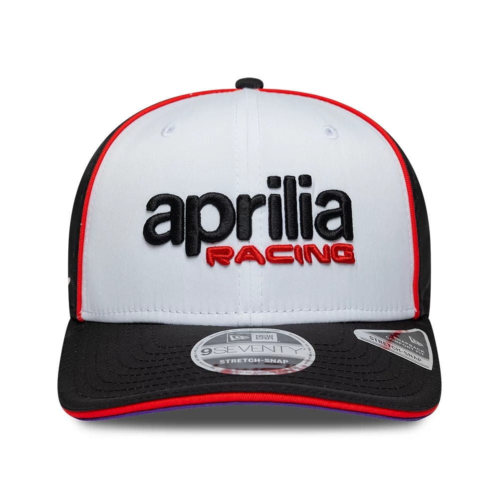 Aprilia Team White New Era 9SEVENTY Stretch Snap Adjustable Cap, front view showing black and red embroidered Aprilia Racing logo on white front panel, with black visor featuring a 9SEVENTY size sticker and red piping along the edges.