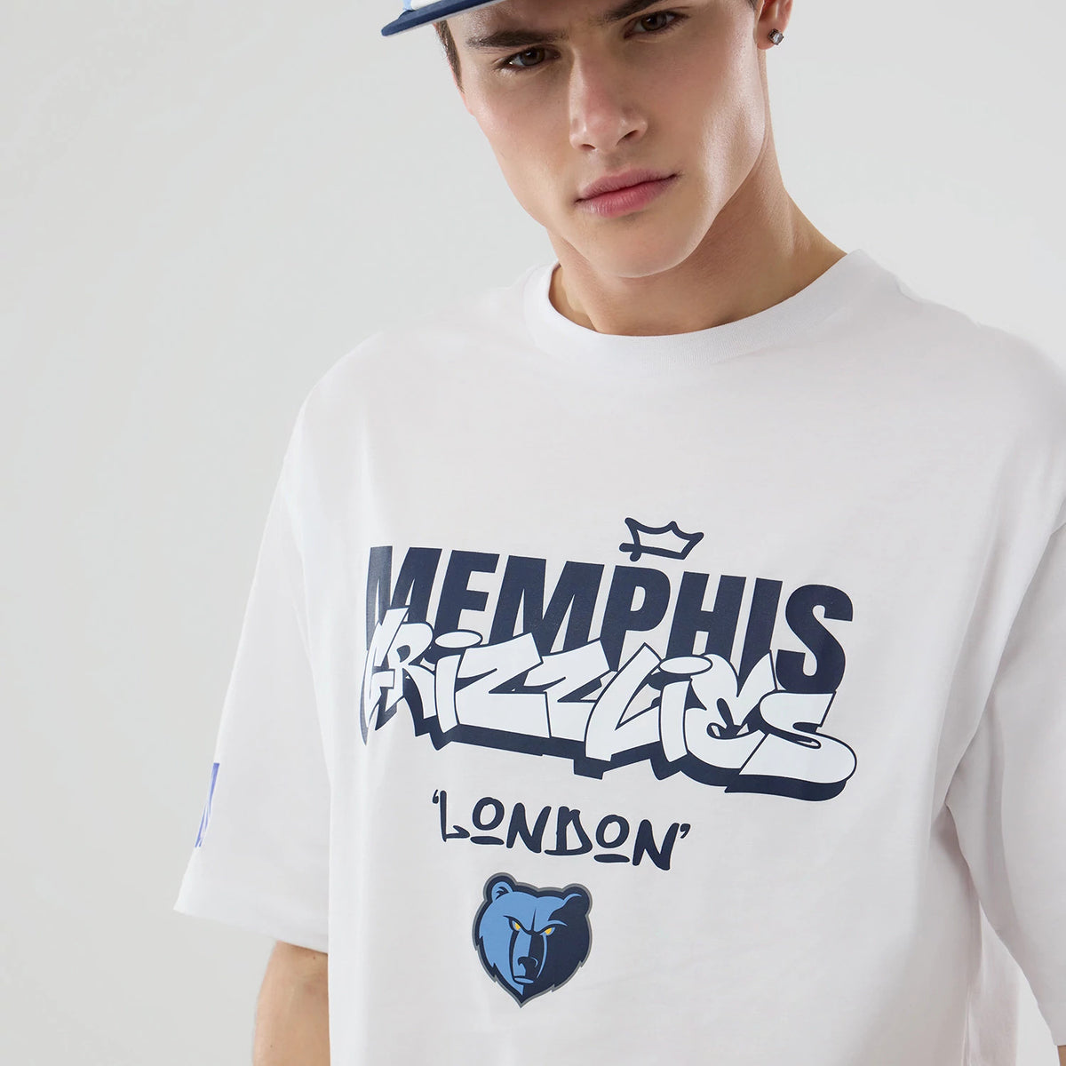 New Era Memphis Grizzlies NBA London Game 2026 White Oversized T-Shirt, front view on-model highlighting a navy graffiti-style Memphis Grizzlies print across the chest with a crown above, and a distinctive bear graphic below the word London.