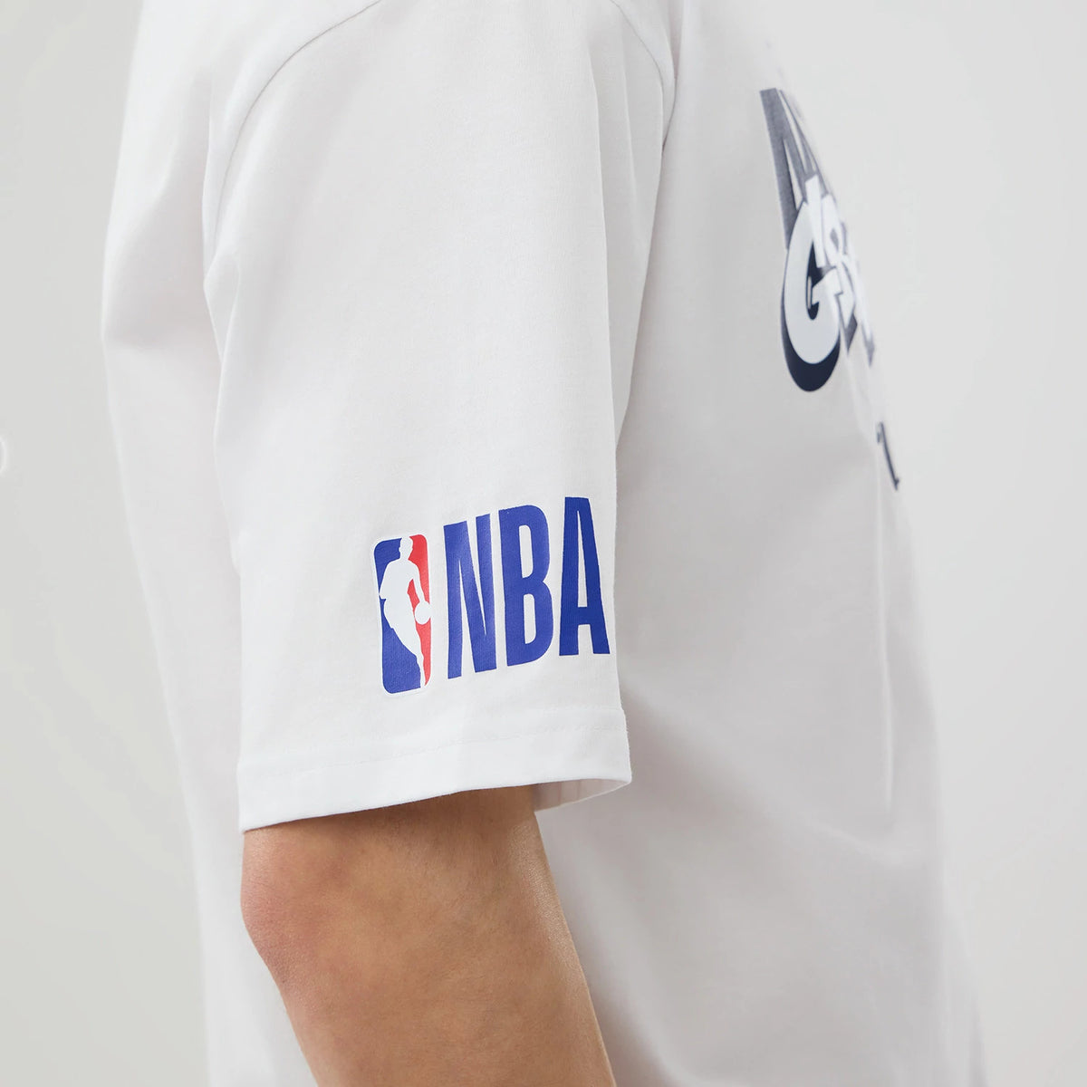 New Era Memphis Grizzlies NBA London Game 2026 White Oversized T-Shirt, side view on a model showcasing a printed NBA logo on the sleeve in red and blue, and a large graphic partially on the back in dark blue and white.