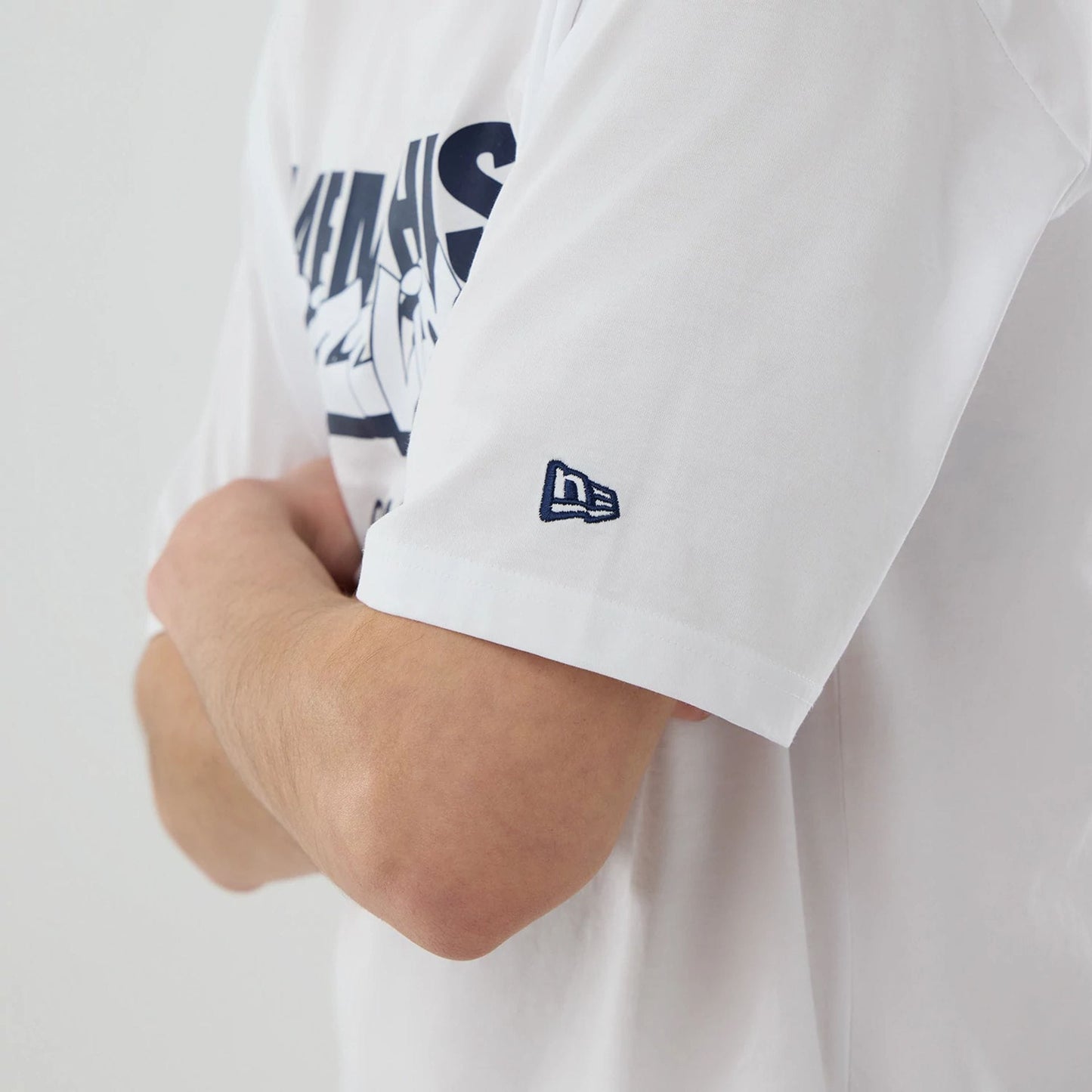 New Era Memphis Grizzlies NBA London Game 2026 White Oversized T-Shirt, three-quarter view showing the navy printed Grizzlies graphic across the chest, worn on a model with crossed arms, and an embroidered New Era flag on the left sleeve.