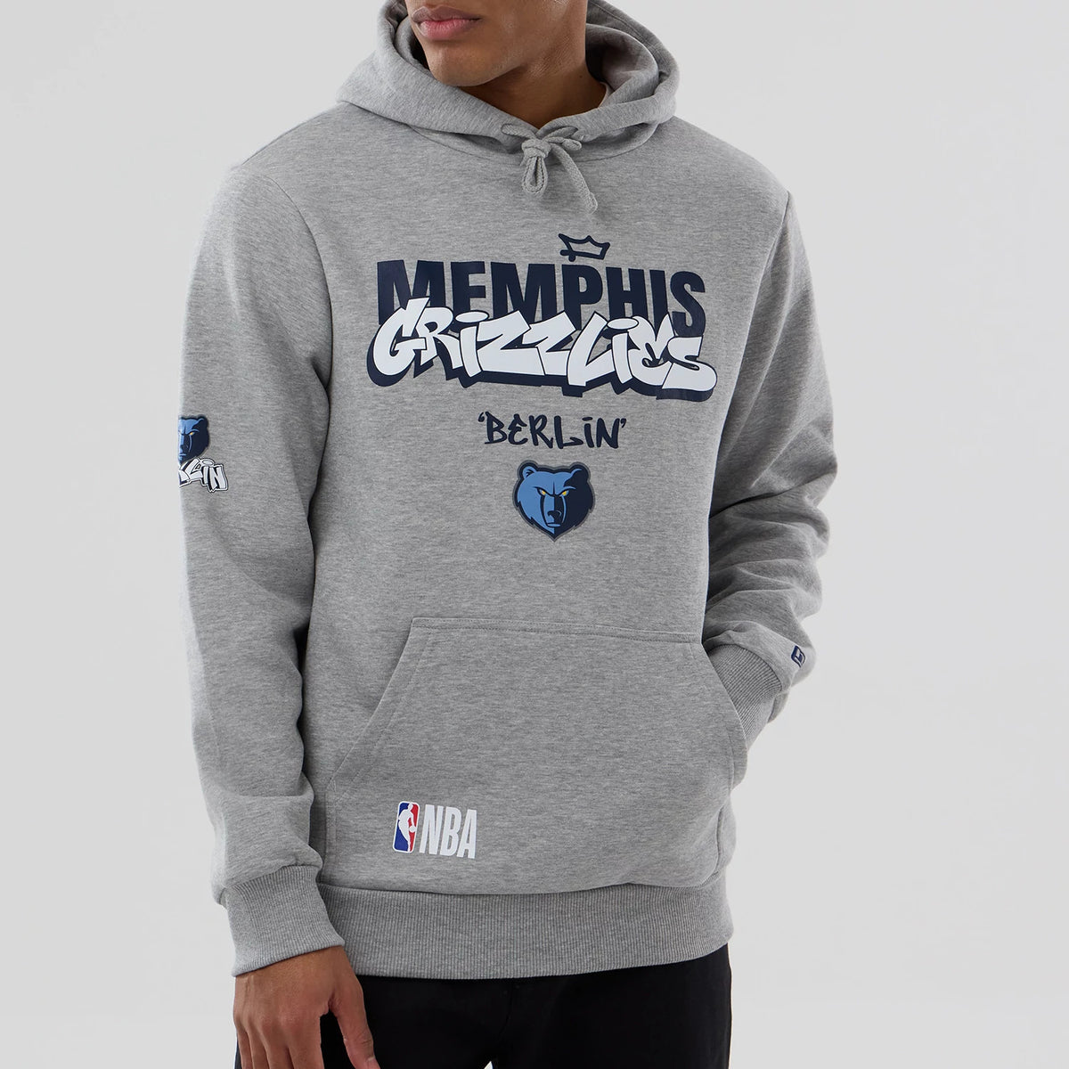 New Era Memphis Grizzlies NBA Berlin Game 2026 Grey Pullover Hoodie, front view on-model featuring navy and white printed Memphis Grizzlies graphics across the chest, the bear logo below, NBA lettering on the pocket, and a small logo on the sleeve.