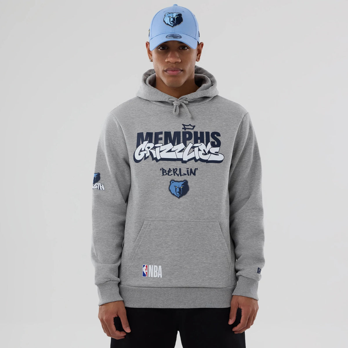 New Era Memphis Grizzlies NBA Berlin Game 2026 Grey Pullover Hoodie, front view on-model showing the large printed Memphis Grizzlies and Berlin graphics across the chest, an embroidered Grizzlies logo on the left sleeve.
