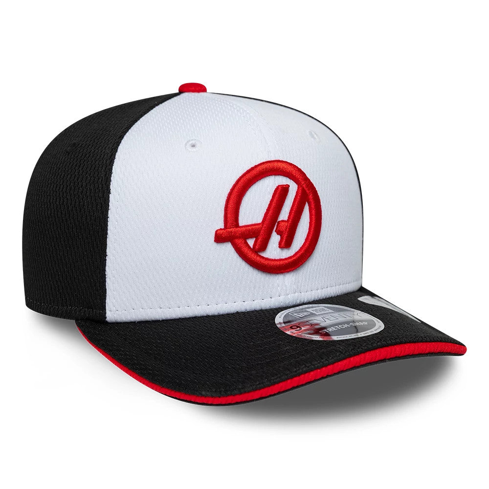 TGR Haas F1 Team Black New Era 9SEVENTY Stretch Snap Adjustable Cap, three-quarter view showing the red embroidered team logo on the front white panel, contrasted with black side panels and visor, featuring a 9SEVENTY size sticker on the visor.