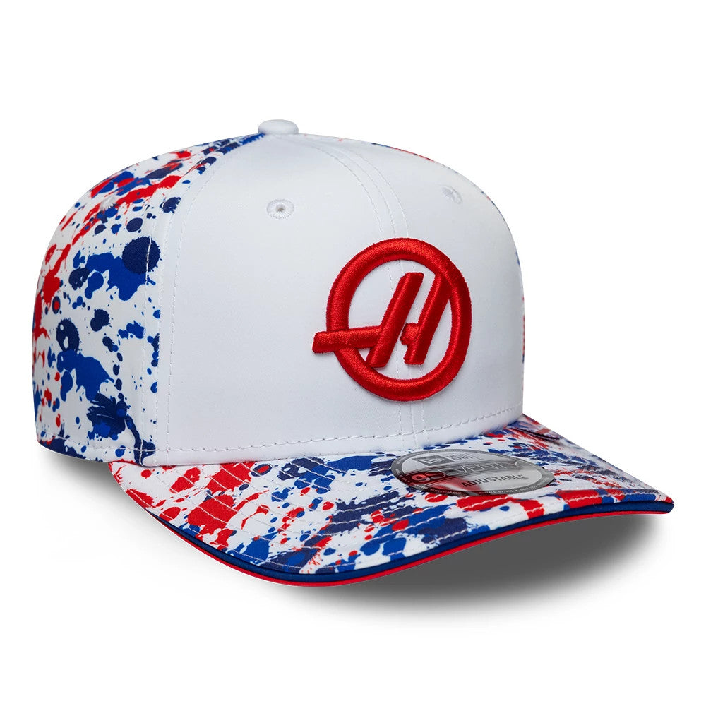 TGR Haas F1 Team Silverstone Race Special White New Era 9SEVENTY Stretch Snap Cap, three-quarter view showing the red embroidered logo on the front panel, with a splatter paint design in blue and red on the visor and side panels.