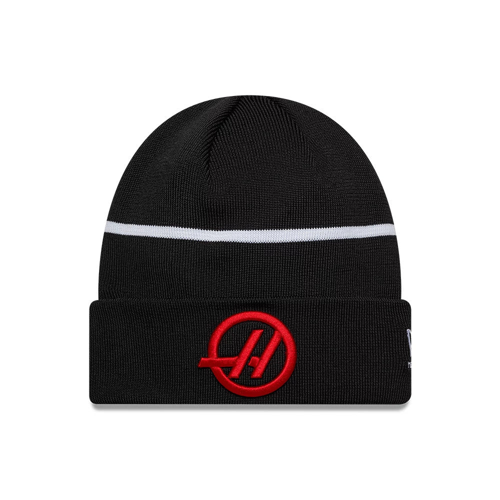 New Era TGR Haas F1 Esteban Ocon Black Cuff Knit Beanie Hat, front view showing a prominent red embroidered A logo on the folded cuff, a horizontal white stripe across the black knit crown, and the New Era flag logo on the side.