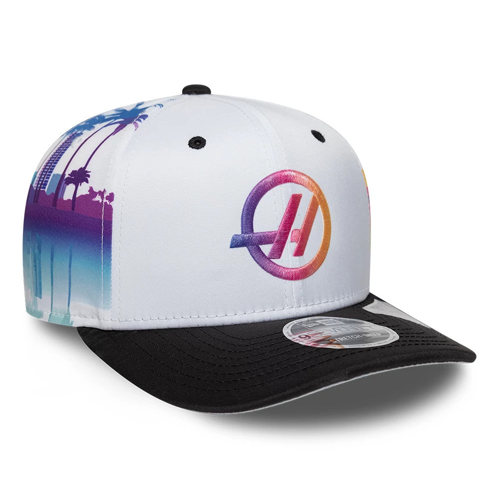 TGR Haas F1 Miami Race Special White New Era 9SEVENTY Stretch Snap Cap, front view showing a multi-coloured embroidered logo on the white front panel, black visor with a 9SEVENTY size sticker, and a skyline design on the side.