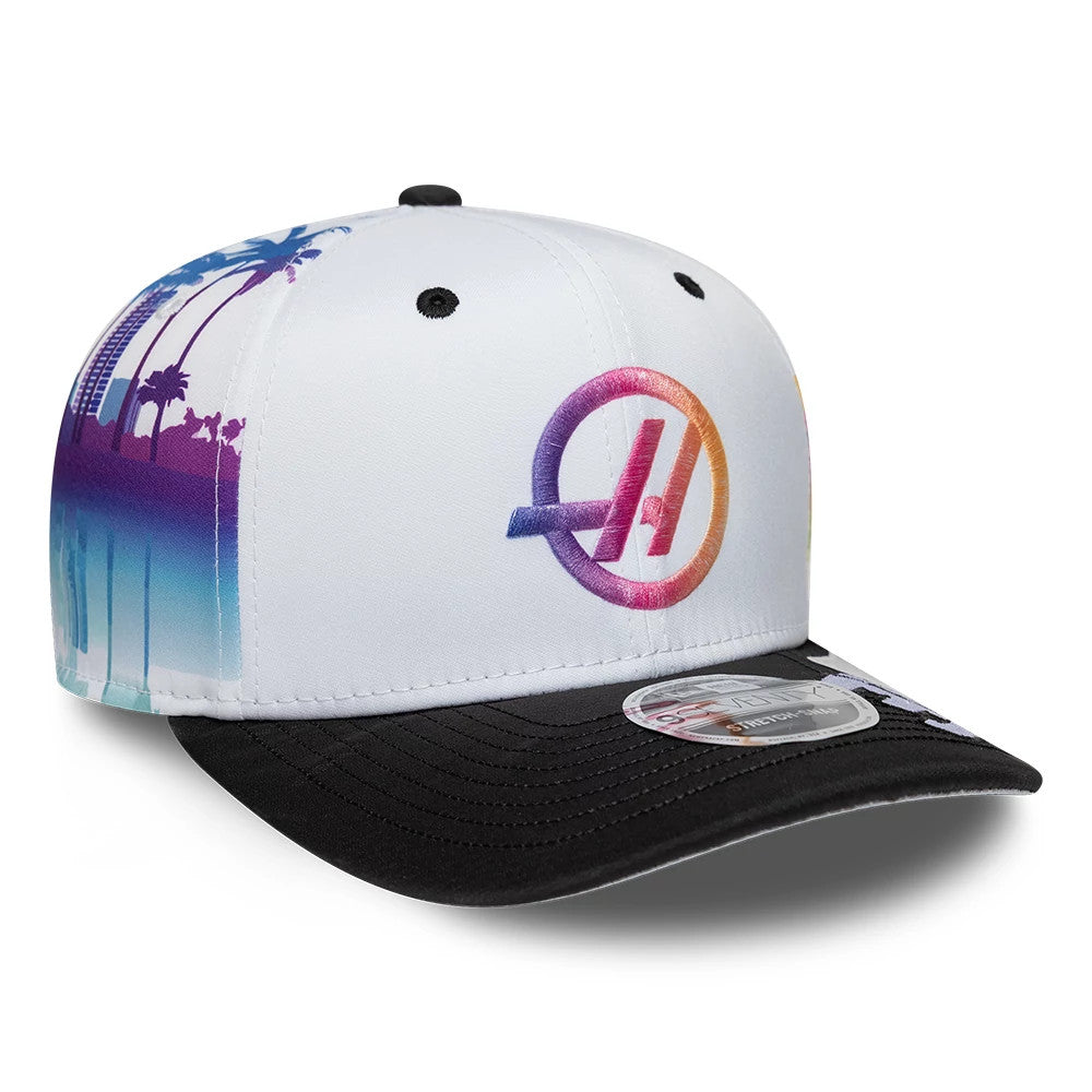 TGR Haas F1 Esteban Ocon Miami Race Special White New Era 9SEVENTY Stretch Snap Cap, three-quarter view showing a multi-coloured embroidered logo on the front panel, a black curved visor with a 9SEVENTY size sticker, and palm tree graphics.