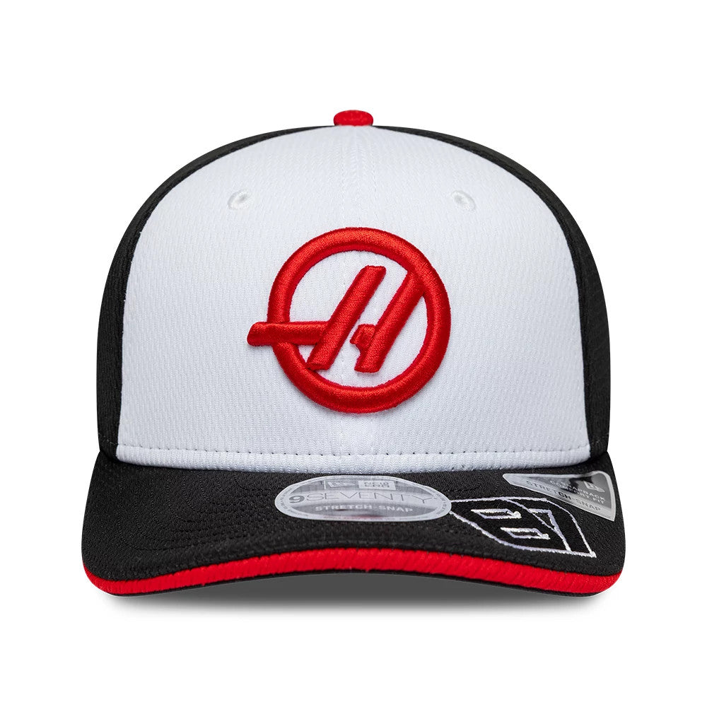 TGR Haas F1 Oliver Bearman Black New Era 9SEVENTY Stretch Snap Cap, front view showing a red embroidered logo on the white front panel, a black visor with red trim, and a 9SEVENTY size sticker on the visor.