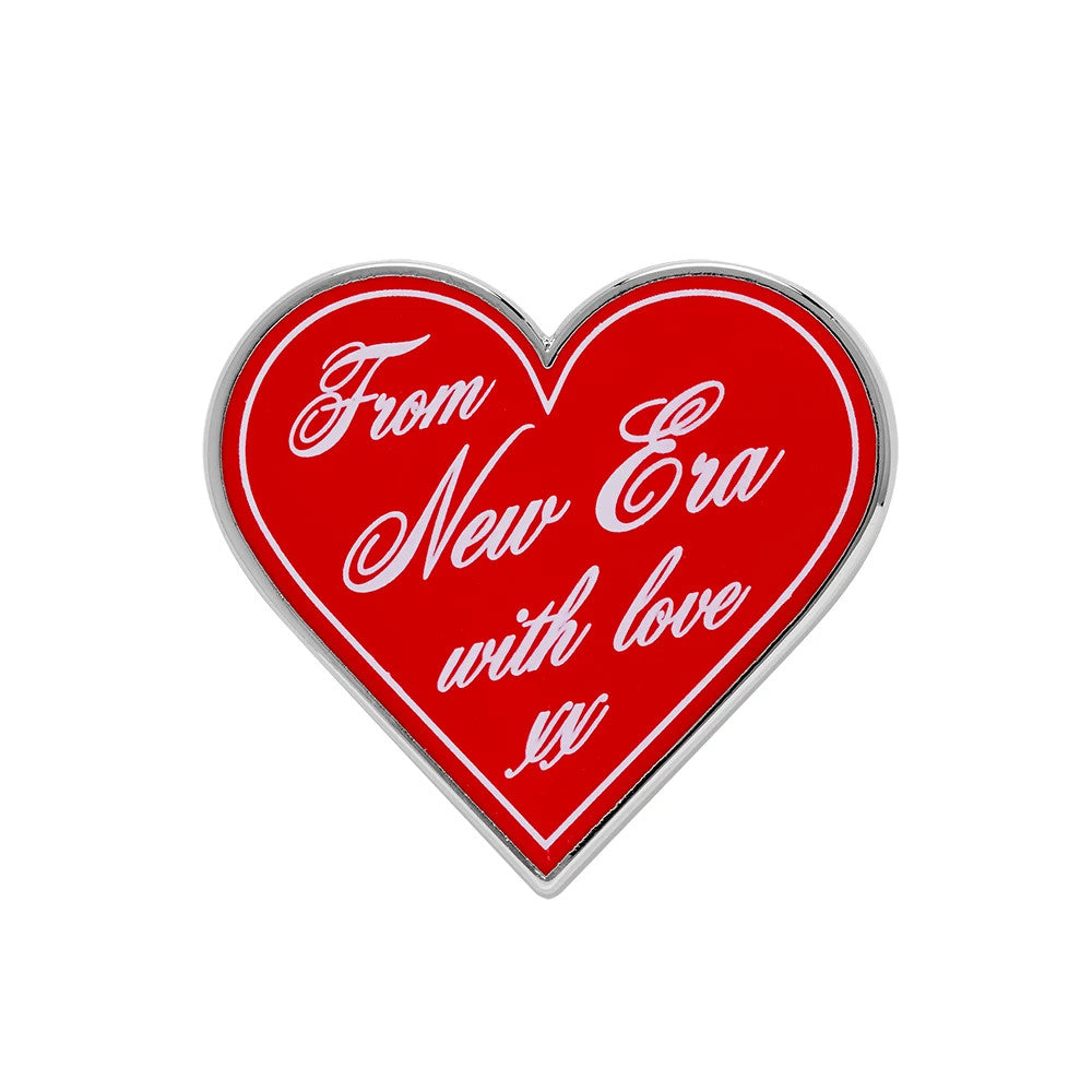 New Era Heart Script Red Pin Badge, front view showing a heart-shaped design with a glossy red finish, featuring white script lettering that reads, From New Era with love xx, bordered by a silver edge for a accent.