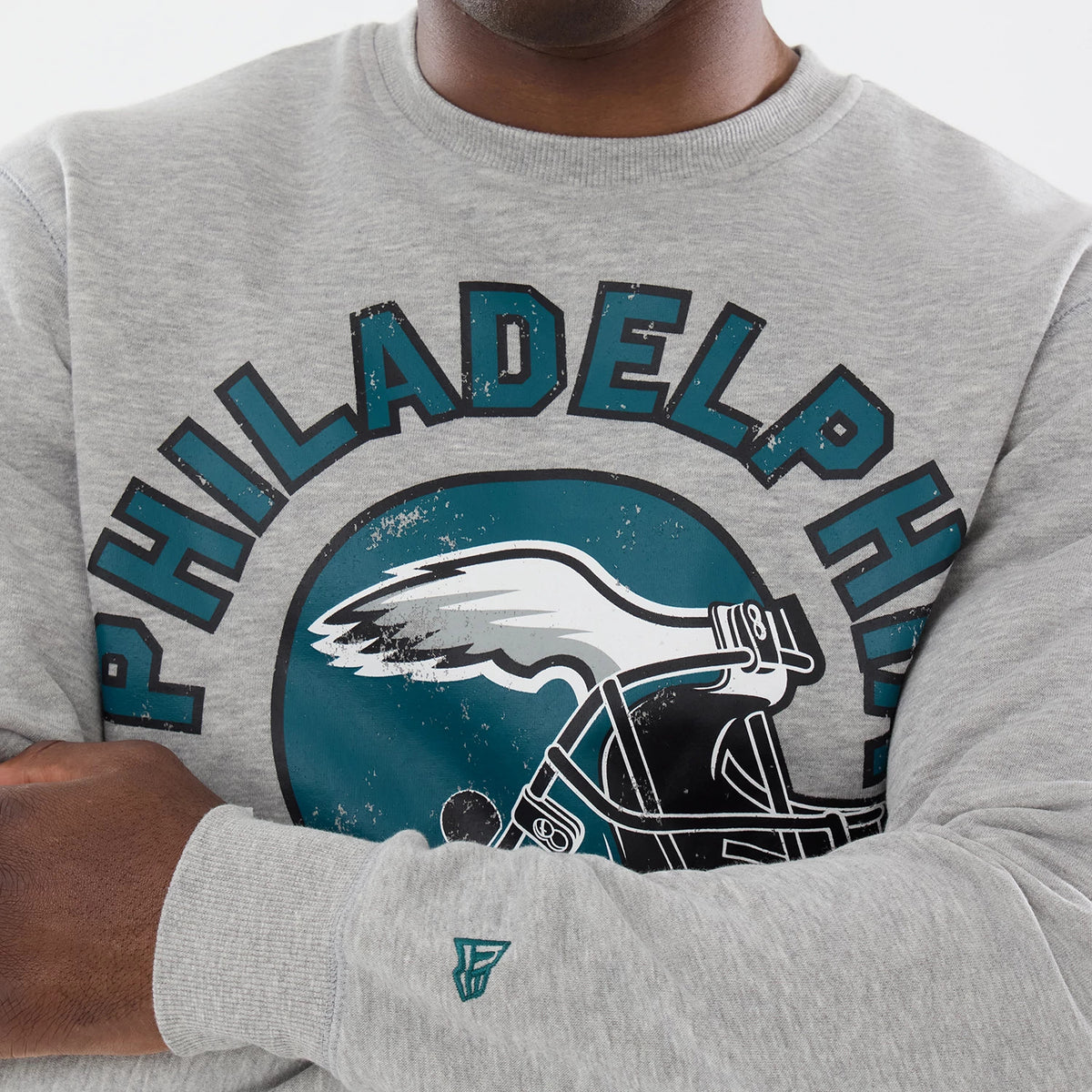 New Era Philadelphia Eagles NFL Training 2026 Grey Crew Neck Sweater, front view on a model with a distressed Philadelphia text and eagle graphic across the chest, featuring a ribbed collar and New Era flag logo embroidered on the sleeve.