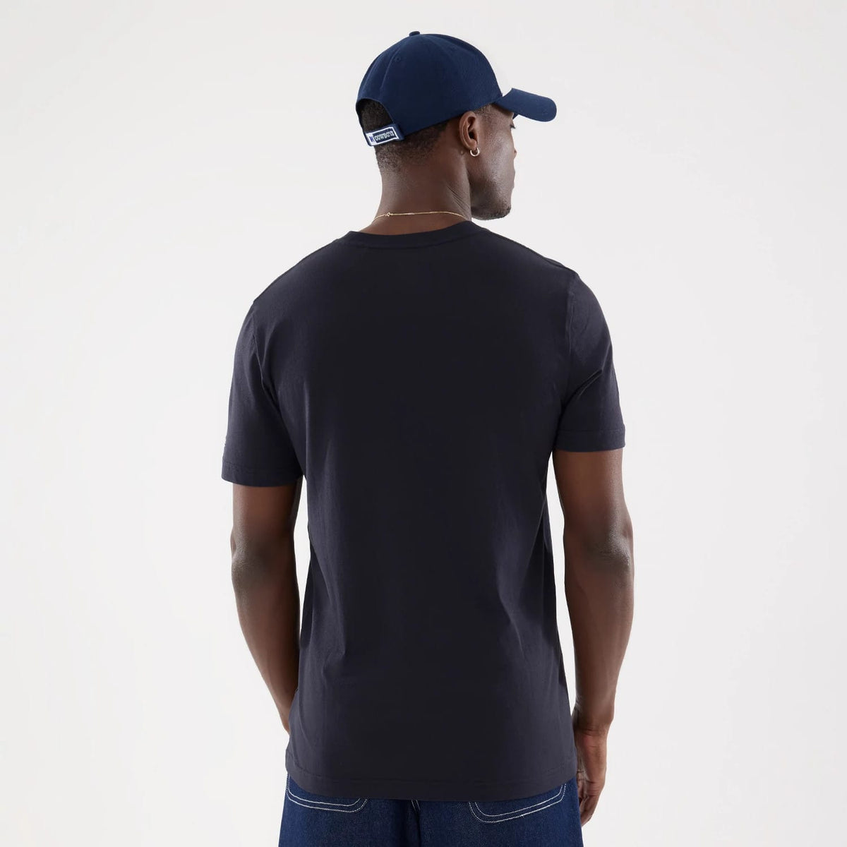 New Era Dallas Cowboys NFL Training 2026 Navy T-Shirt, back view on a model wearing a navy cap, showing a plain navy back with short sleeves and the shirt's relaxed fit, paired with dark jeans for a casual style.