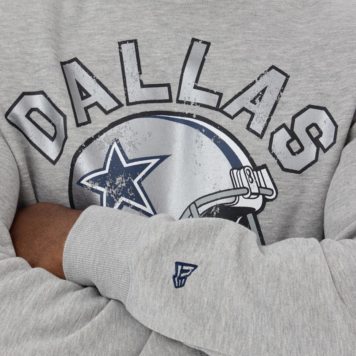 New Era Dallas Cowboys NFL Training 2026 Grey Crew Neck Sweater, close-up showing distressed printed Dallas Cowboys helmet graphic in dark blue and grey on the chest, with navy blue embroidered New Era logo on the left sleeve.