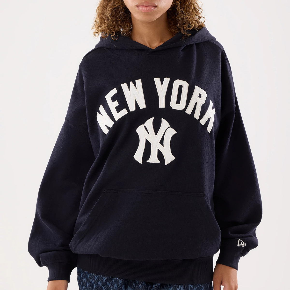 New Era New York Yankees Womens MLB Navy Oversized Pullover Hoodie, front view on a model showing large white embroidered New York lettering and Yankees logo on the chest, a spacious kangaroo pocket.