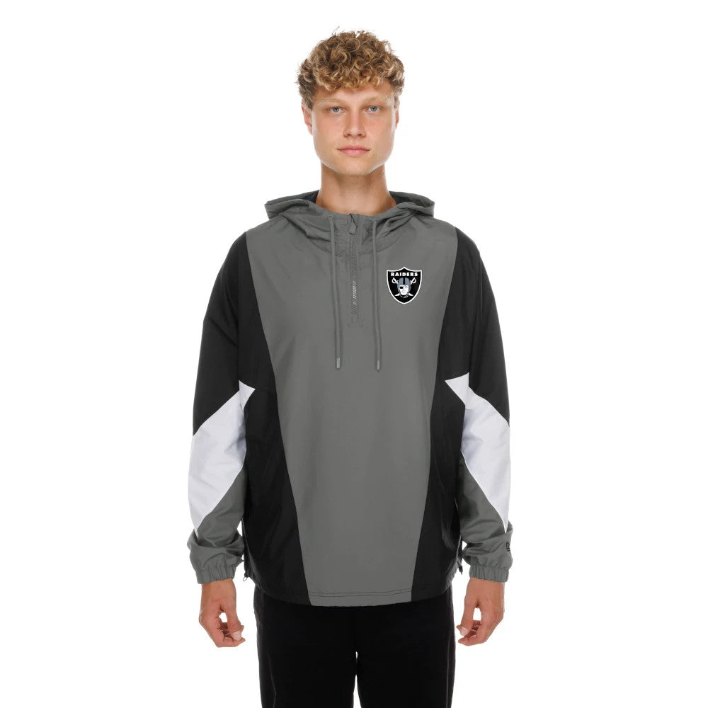 New Era Las Vegas Raiders NFL Grey Windbreaker Jacket, front view showing a grey jacket with a hood and drawstrings, black and white panels on the sleeves, and an embroidered Raiders shield logo on the left chest, worn by a model in black trousers.