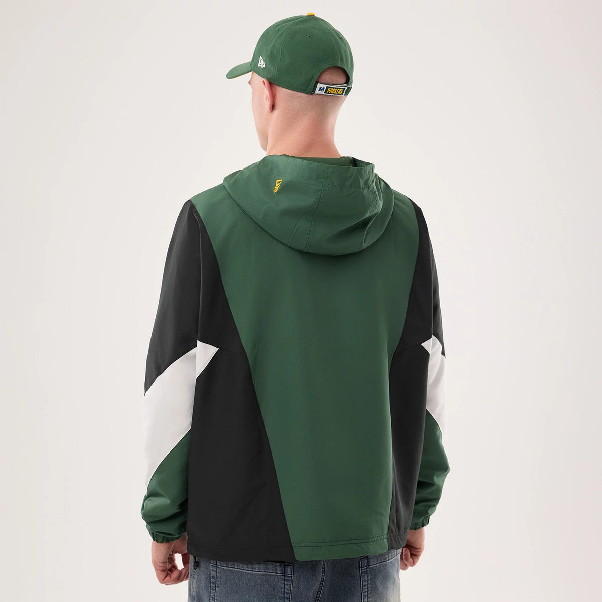 New Era Green Bay Packers NFL Dark Green Jacket, back view on a model showcasing the green hood and upper back with a small embroidered team logo, contrasted by black and white panels on the sleeves and a matching cap.
