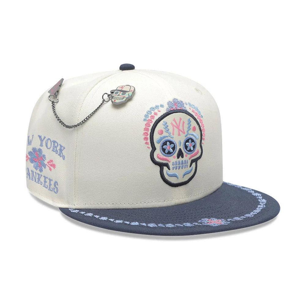 Yankees MLB Day Of The Dead Light Beige & Dark Blue New Era 59FIFTY Fitted Cap, three-quarter view showing the colourful sugar skull graphic with pink and blue embroidery on the front panel, dark blue visor with floral decoration.