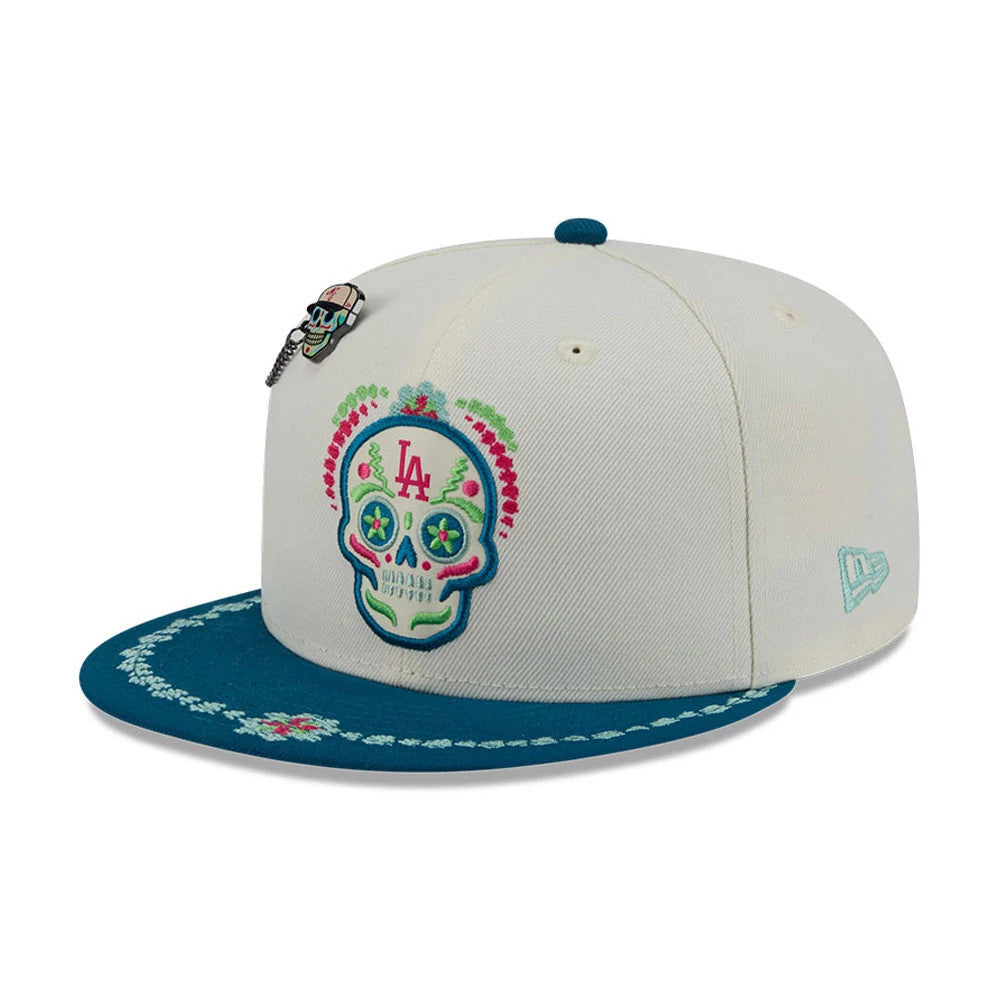 LA Dodgers MLB Day Of The Dead Light Beige & Blue New Era 59FIFTY Fitted Cap, three-quarter view showing a colourful embroidered sugar skull with LA letters on the front panel, teal visor with decorative floral stitching, and the New Era flag logo.