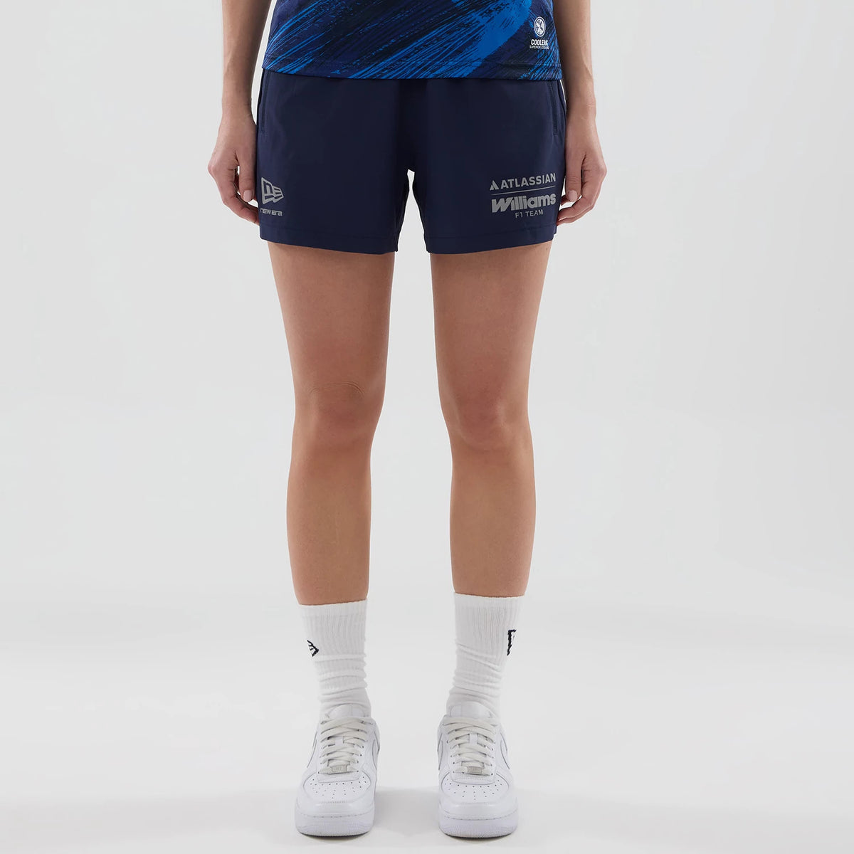 New Era Williams Womens Navy Training Shorts, front view on a model showing New Era and Williams F1 Team logos printed on the lower left and right sides, respectively, styled with white socks and trainers.