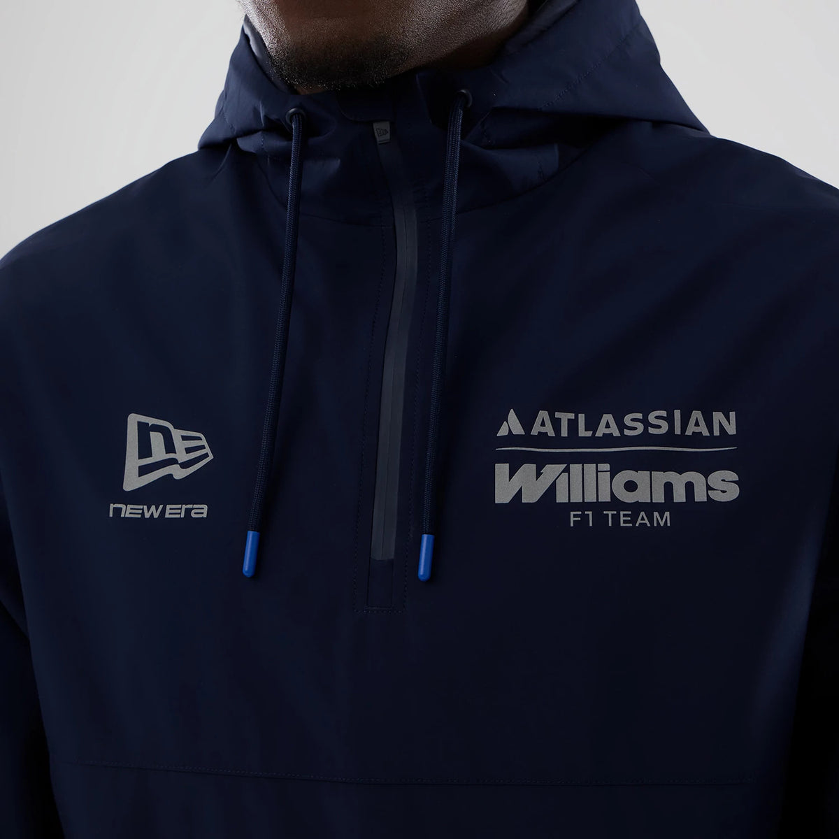 New Era Williams Navy Windbreaker Jacket, front view showing the dark blue fabric with a New Era embroidered logo on the left chest, the Atlassian and Williams F1 Team printed logos on the right chest, and a zip with blue tips.
