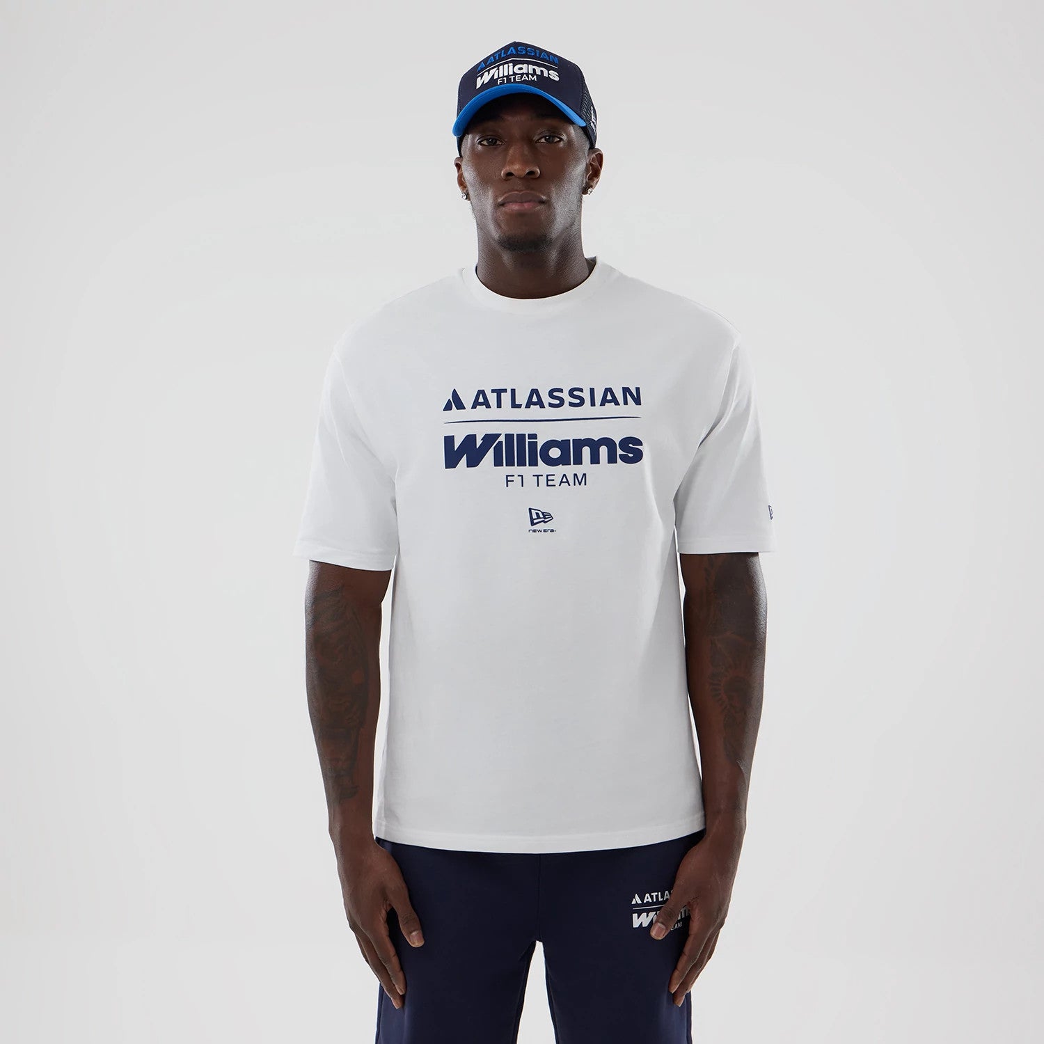 New Era Williams White Oversized T-Shirt, front view on a model styled with a matching cap, featuring navy blue Atlassian and Williams F1 Team lettering across the chest, and a small embroidered New Era logo below the text.
