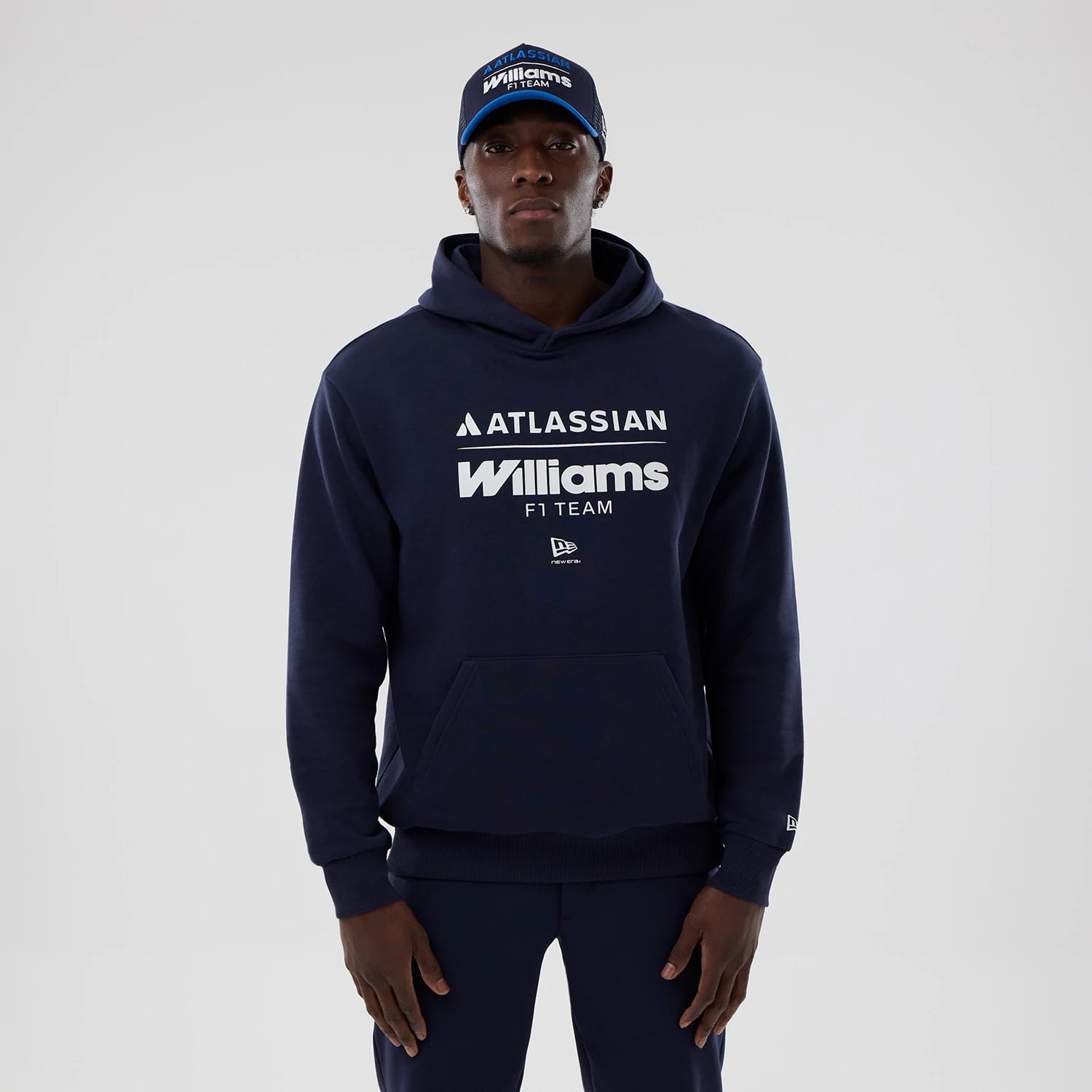 New Era Williams Navy Oversized Pullover Hoodie, front view on-model featuring large white printed Atlassian and Williams F1 Team logos across the chest, a kangaroo pocket at the lower front, and a small embroidered New Era logo on the sleeve cuff.
