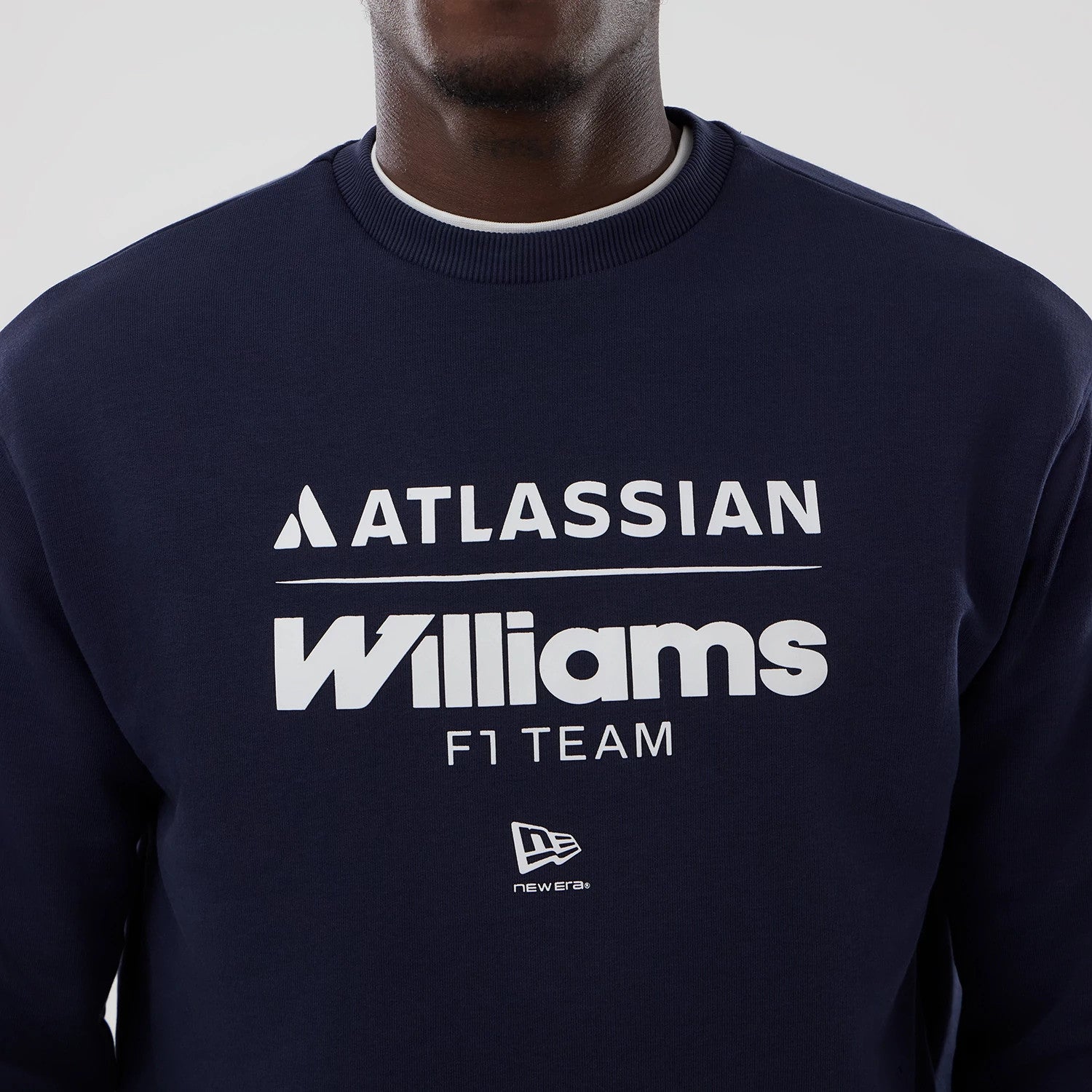 New Era Williams Navy Oversized Crewneck Sweater, front view on a model displaying white Williams F1 Team and Atlassian logos across the chest, with a small New Era flag logo positioned below, all set against the deep navy fabric.