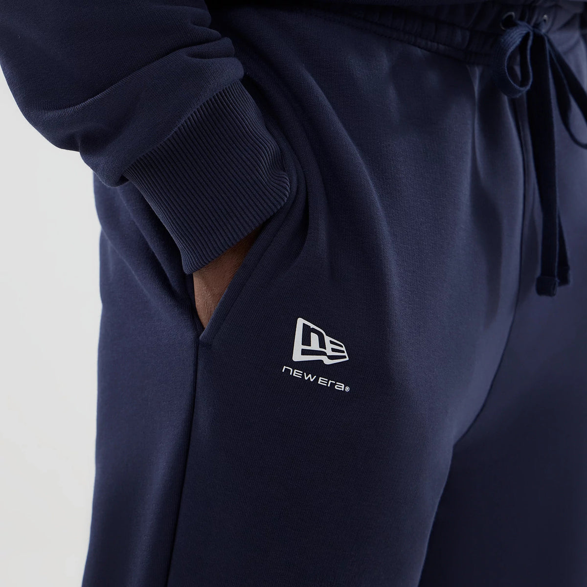 New Era Williams Navy Joggers, close-up view showing the New Era flag logo in white on the left thigh, with ribbed cuffs at the ankle, and a drawstring waist for adjustable fit, crafted in a deep navy blue fabric.