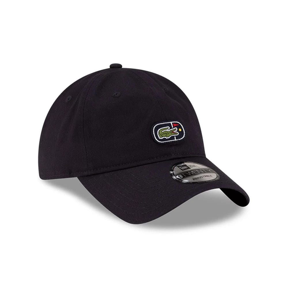 Lacoste X New Era Navy 9TWENTY Adjustable Cap, three-quarter view showing the embroidered Lacoste crocodile logo on the front panel, the curved navy visor with a 9TWENTY size sticker, and the round top button with eyelets on the crown.