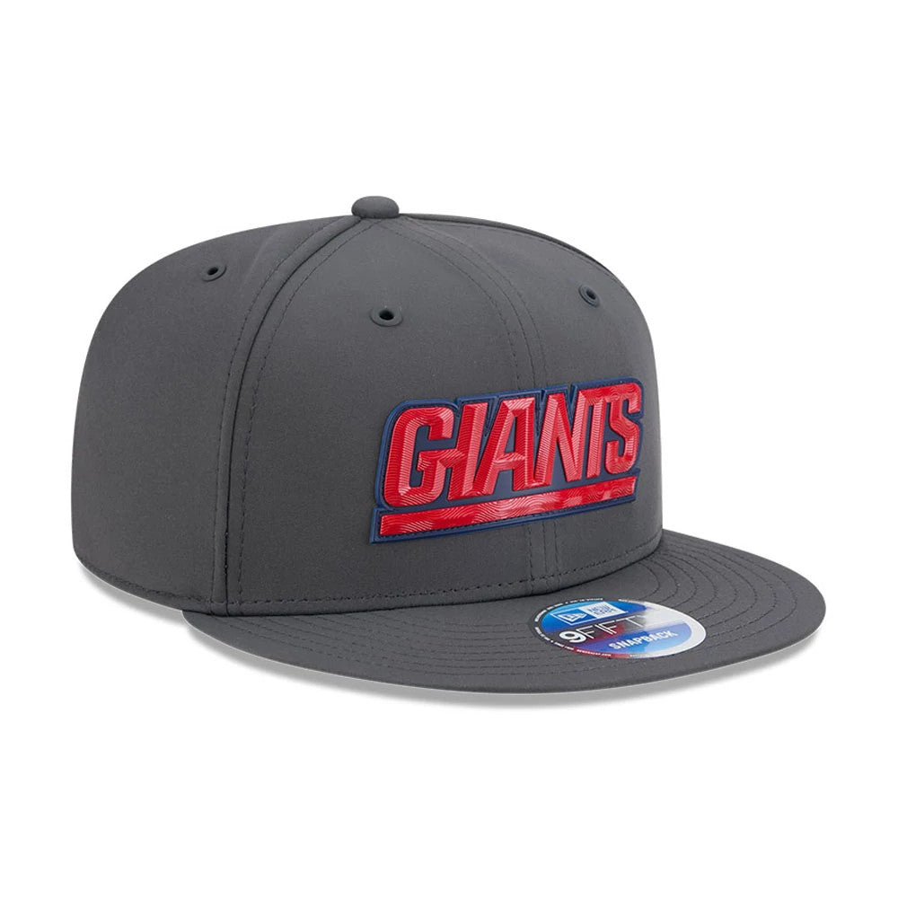 New York Giants NFL Sideline 2026 Charcoal New Era 9FIFTY Snapback Adjustable Cap, front view showing raised red and blue embroidered GIANTS lettering on the structured charcoal front panel, with a flat visor and a 9FIFTY size sticker.