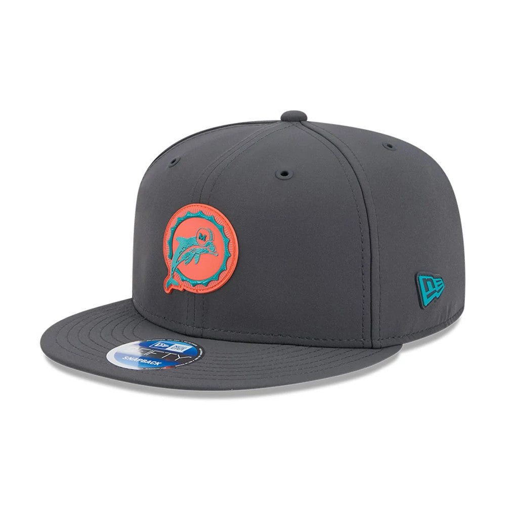Miami Dolphins NFL Sideline 2026 Charcoal New Era 9FIFTY Snapback Adjustable Cap, three-quarter view showing the raised orange and teal embroidered Dolphins logo on the front panel, a matching teal New Era flag logo on the left side.