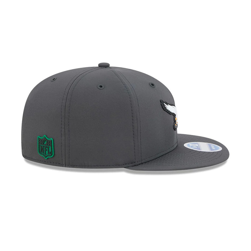 Eagles NFL Sideline 2026 Charcoal New Era 9FIFTY Snapback Adjustable Cap, side view showing the raised white and black eagle logo on the front panel, a green NFL shield logo on the right side, and a flat charcoal visor.