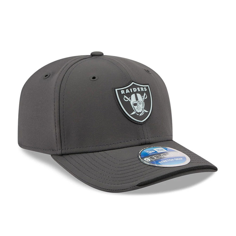 Raiders NFL Sideline 2026 Charcoal New Era 9SEVENTY Stretch Snap Adjustable Cap, three-quarter view showing a light grey Raiders shield logo embroidered on the structured charcoal front panel, a black curved visor and a 9SEVENTY size sticker.