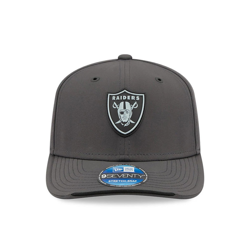 Raiders NFL Sideline 2026 Charcoal New Era 9SEVENTY Stretch Snap Adjustable Cap, front view showing a raised silver and black Raiders shield logo on the grey front panel, charcoal flat visor, and blue 9SEVENTY size sticker on the visor.