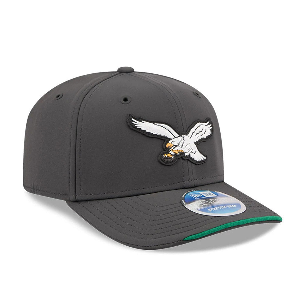 Eagles NFL Sideline 2026 Charcoal New Era 9SEVENTY Stretch Snap Adjustable Cap, three-quarter view showing a raised embroidered eagle logo in white and black on the front panel, a dark charcoal structured crown.
