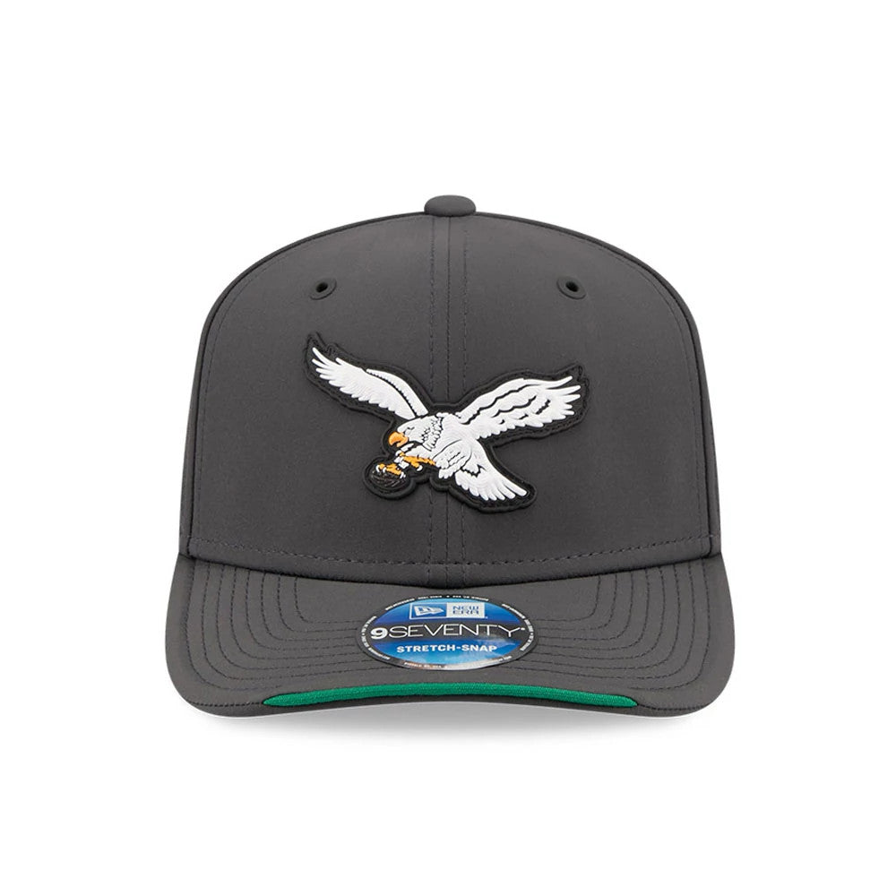 Eagles NFL Sideline 2026 Charcoal New Era 9SEVENTY Stretch Snap Adjustable Cap, front view showing a raised embroidered eagle logo on the front panel, paired with a flat charcoal visor and a 9SEVENTY size sticker, featuring green under the visor.