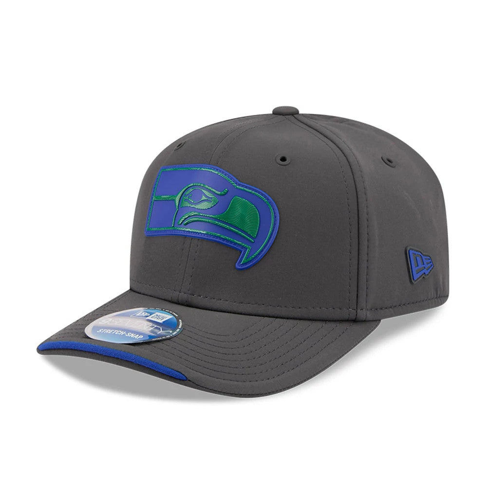 Seahawks NFL Sideline 2026 Charcoal New Era 9SEVENTY Stretch Snap Adjustable Cap, front view showing a raised blue and green embroidered Seahawks logo on the structured charcoal crown, with a blue-edge charcoal visor and a 9SEVENTY size sticker.