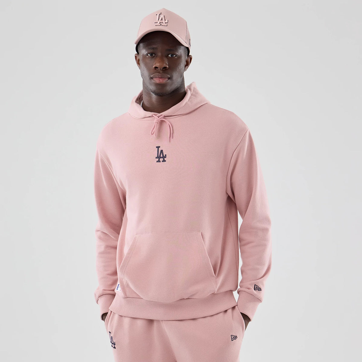 New Era Dodgers MLB Midi League Essential Pastel Pink Oversized Pullover Hoodie, front view on a model showing an embroidered LA logo in black on the centre chest, with drawstring fastening at the neck and a New Era flag embroidered on the cuff.